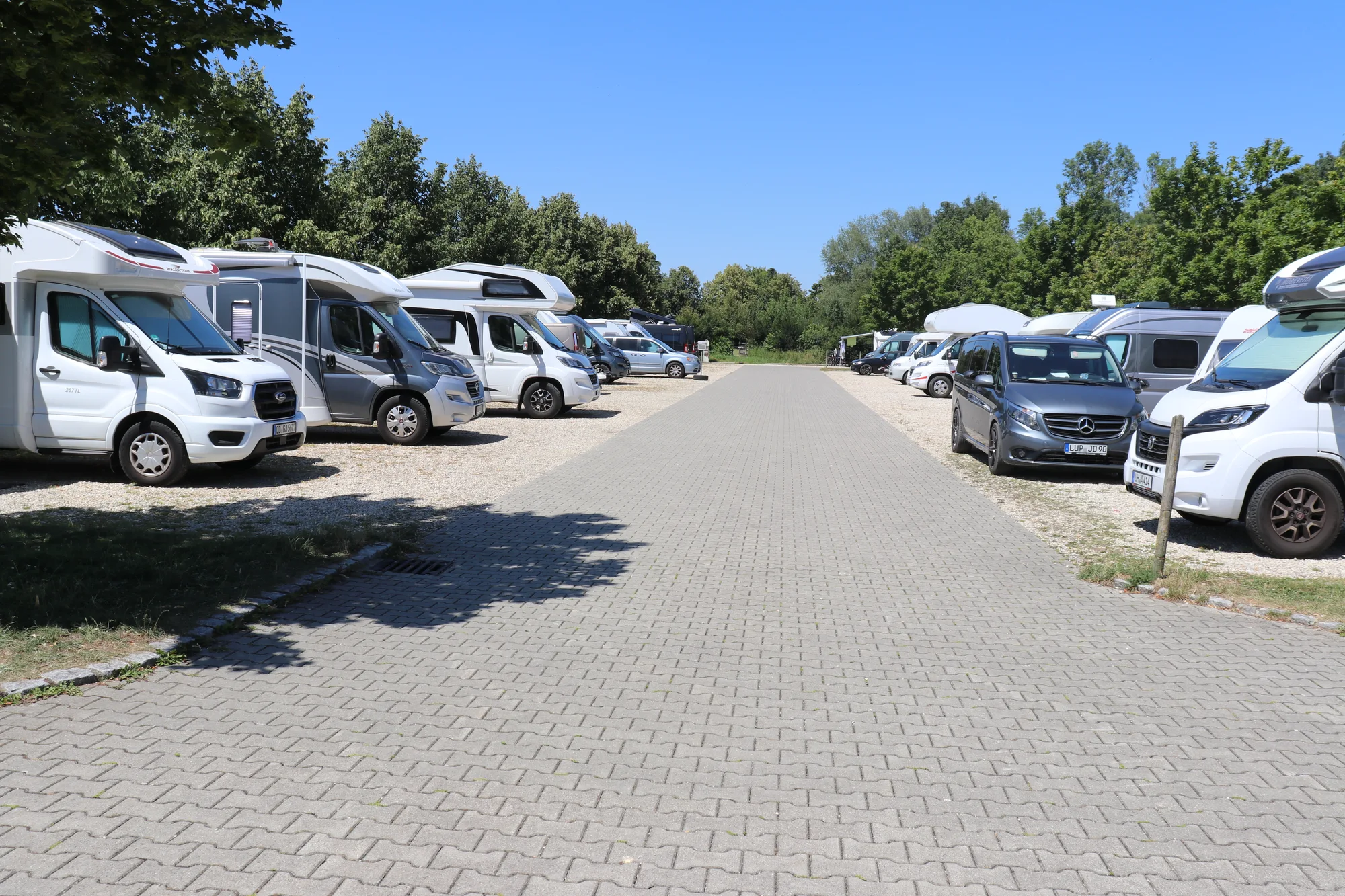 Gepflasterte Fahrgasse im Wohnmobilpark Erding mit belegten Stellplätzen zu beiden Seiten