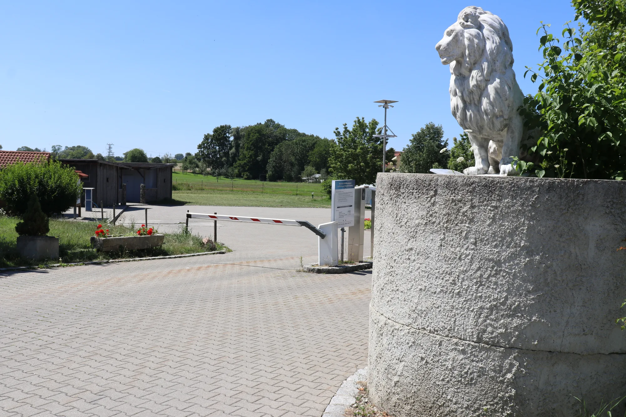 Steinlöwe auf einem Sockel an der Einfahrt zum Wohnmobilpark Erding, dahinter die Schranke