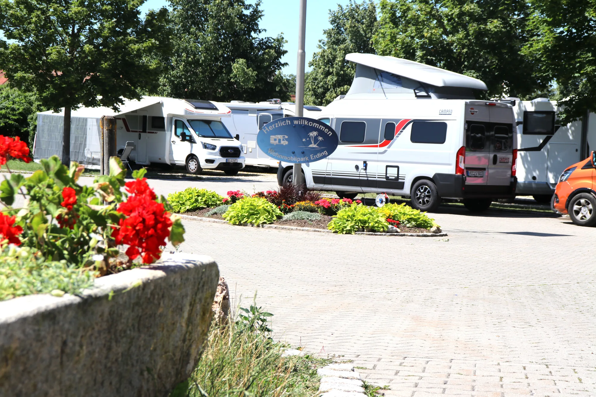 Wohnmobile mit ausgefahrener Markise an der bepflanzten Blumeninsel im Wohnmobilpark Erding