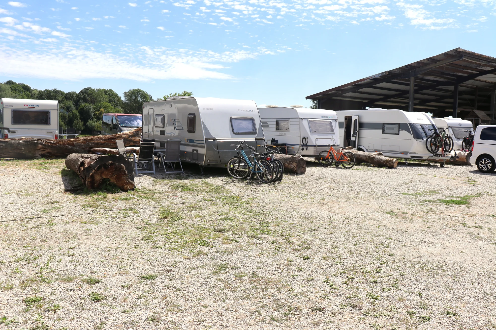 Wohnwagen mit Fahrrädern auf dem Kiesplatz, rechts eine überdachte Stellfläche