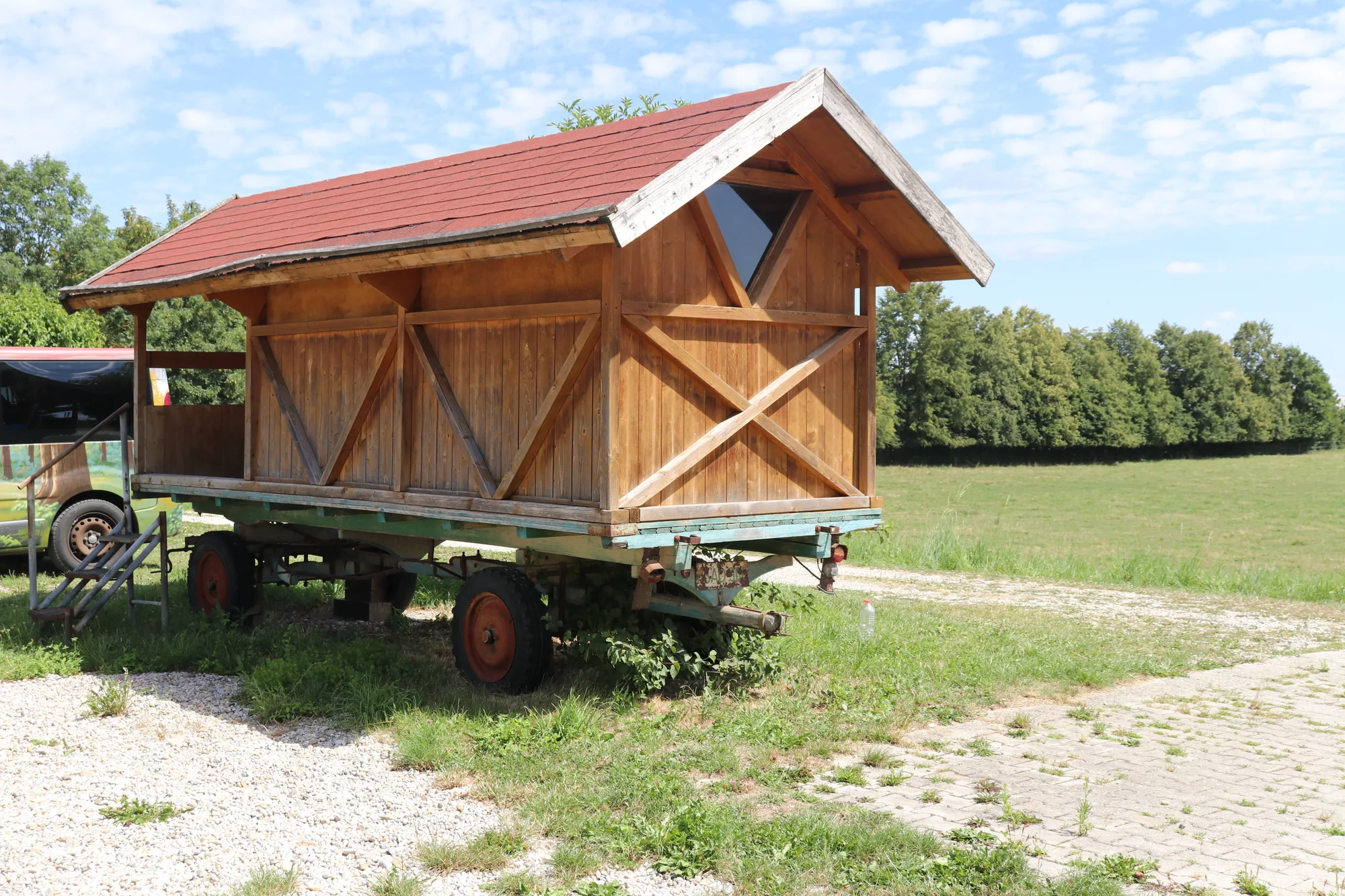 Historischer Holzwagen mit Satteldach auf einem Anhänger neben der Wiese