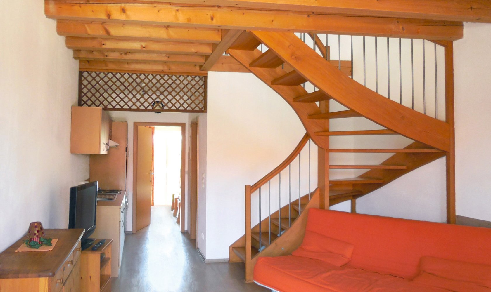 Wohnraum einer Ferienwohnung am Gersthof mit hölzerner Galerietreppe und rotem Sofa